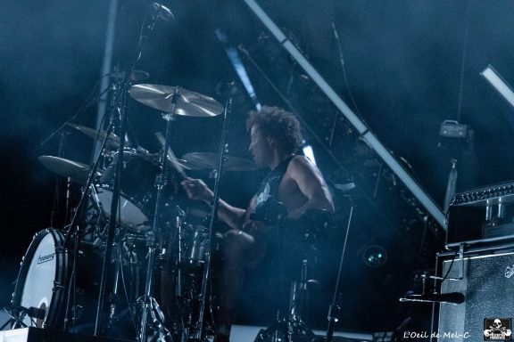 A drummer performing on stage with a smoky background and dramatic lighting.