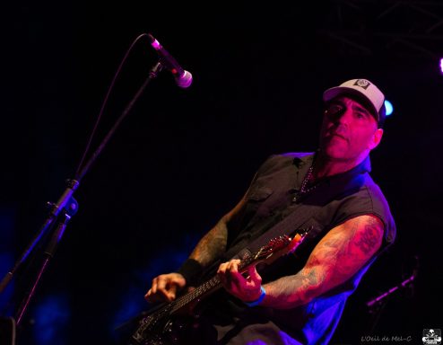 A musician playing guitar on stage with microphones in the foreground.