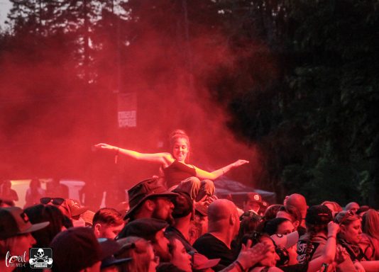 A crowd at a concert, with a person on someone's shoulders surrounded by red light.