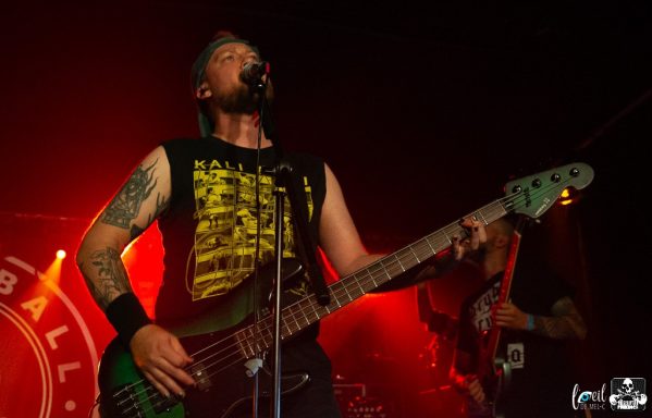 Musician playing a green bass guitar on stage with vibrant red lighting.