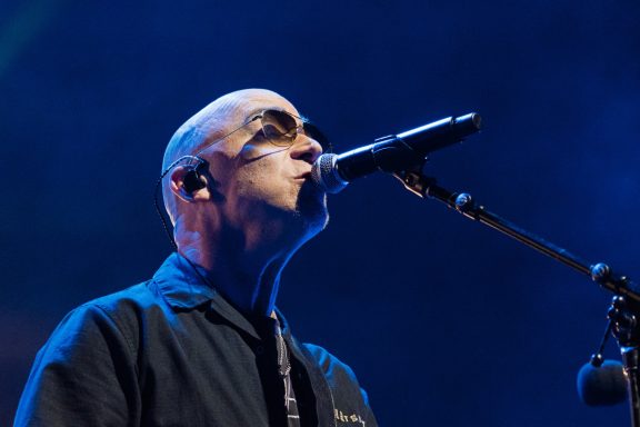 +LIVE+ - Centre Videotron Musician with sunglasses performing at a microphone under dramatic lighting.