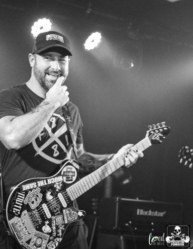 Smiling guitarist performs on stage with a decorated electric guitar.