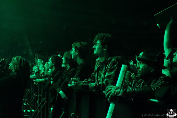 Crowd at a concert under green lighting, some people holding up signs.