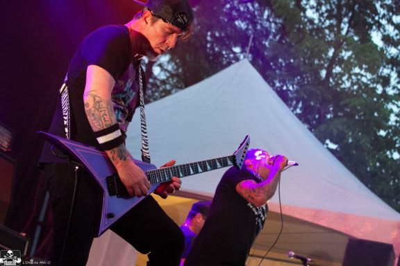 Musicians performing on stage, one playing guitar and the other singing passionately.