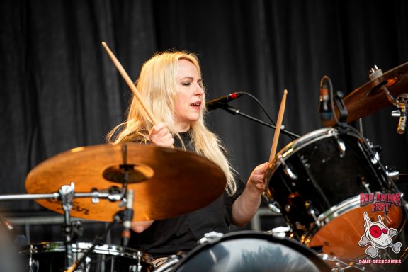 Drummer performing live on stage with focused expression and drumsticks raised.