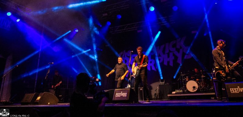 A band performs on stage with colorful lighting and enthusiastic crowd participation.