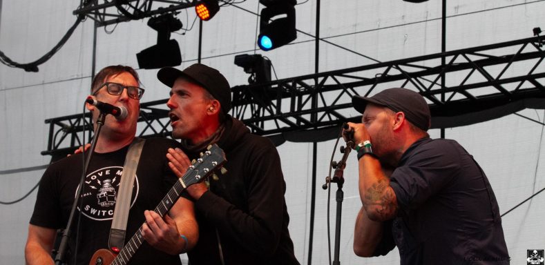 Three musicians perform on stage with guitars and microphones at a live concert.