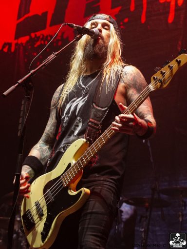 Musician with long hair and tattoos playing an electric bass on stage.