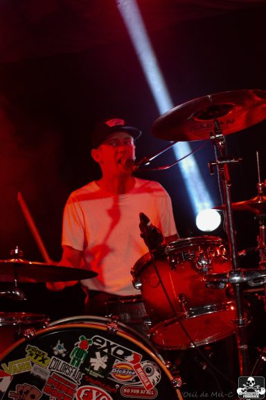 Drummer performing on stage with dramatic lighting and energetic atmosphere.