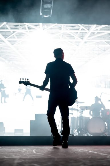 Bryan Adams - Canada Silhouette of a guitarist on stage, with lights and band members in the background.