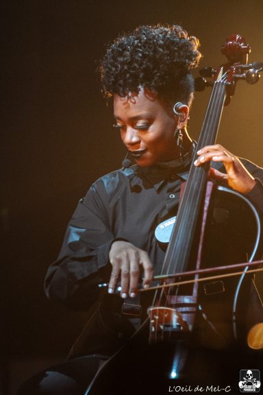 A musician plays the cello on stage, focused and immersed in the performance.