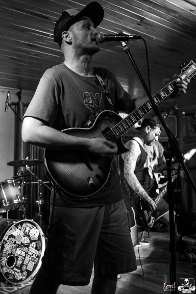 Musician performing with a guitar on stage, singing into a microphone.