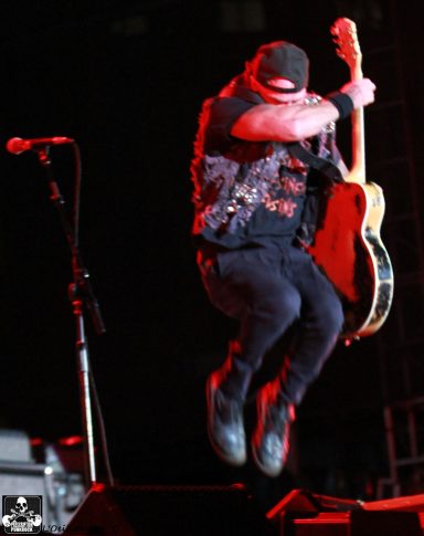 A musician jumps while playing guitar on stage, with enhanced stage lighting effects.