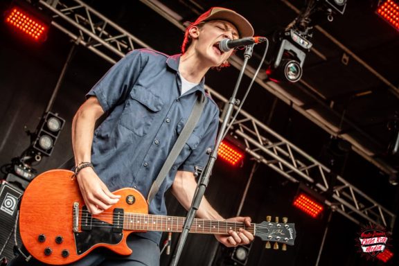 A musician performing on stage with an electric guitar and microphone.