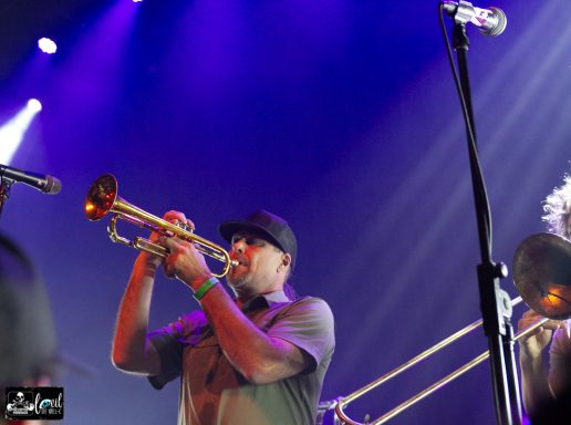 Musician playing the trombone on stage with vibrant lighting in the background.