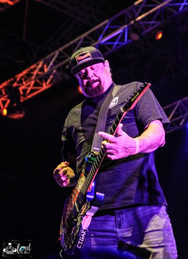 Musician passionately playing electric guitar on stage with vibrant lighting.