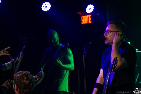 Band performing on stage with dramatic lighting and an engaged audience.