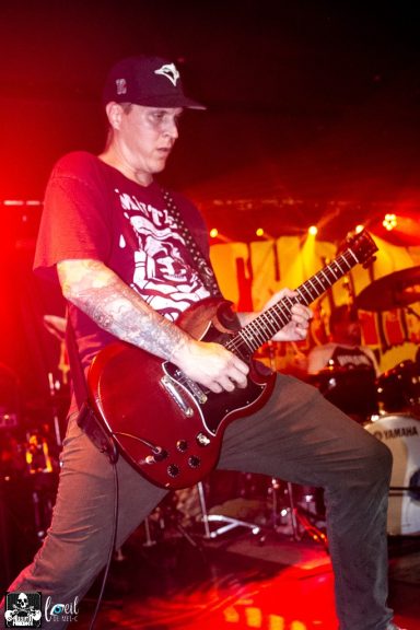 Musician playing electric guitar on stage with dramatic lighting.