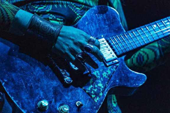 The Damn Truth - Centre Videotron Close-up of a musician's hand playing a blue electric guitar.