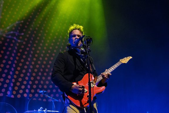 Big Wreck - Centre Videotron Performer singing into a microphone while playing an orange electric guitar on stage.