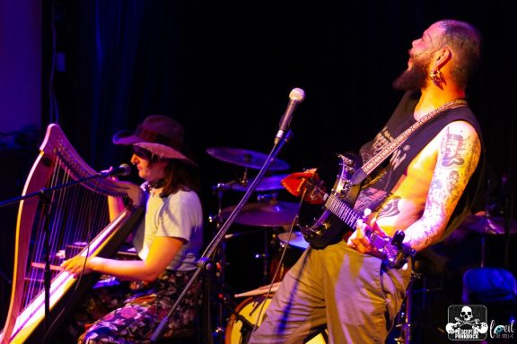 Musicians performing live, one on harp and another on guitar, with an energetic atmosphere.