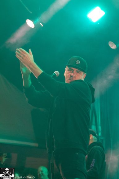 A performer claps enthusiastically on stage under green lighting.