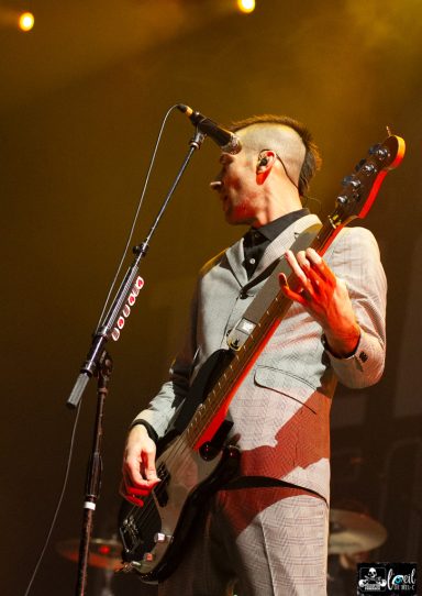 A man in a suit plays a bass guitar on stage with a microphone.
