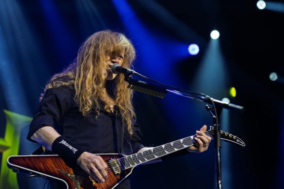 Musician with long hair playing guitar and singing on stage.