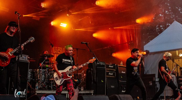 A band performs on stage with orange lights and energetic crowd.