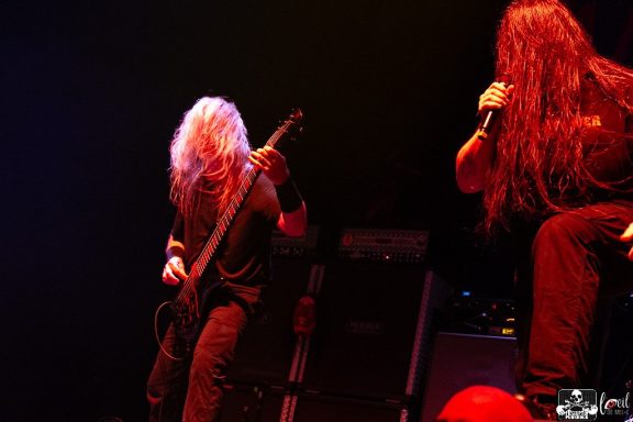 Musicians performing on stage, one playing guitar and the other singing passionately.