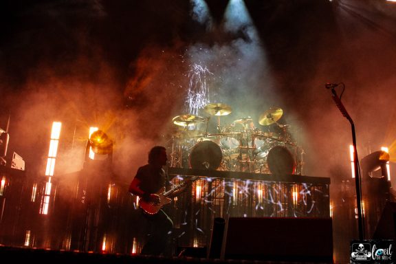 Musician performing on stage with drums and vibrant lighting effects.