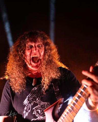 Man with curly hair passionately performing on stage with a guitar.