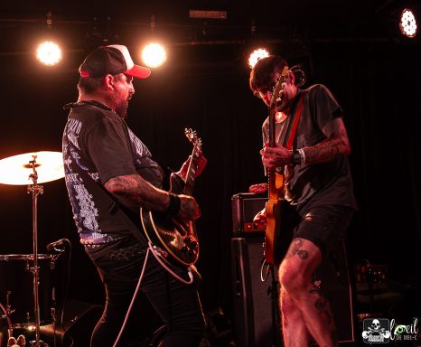 Two musicians performing on stage, one playing guitar and the other on bass.