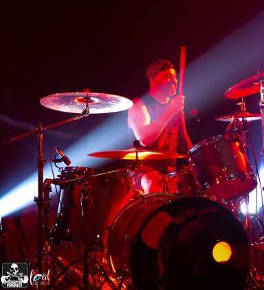 Drummer performing on stage with bright stage lights and dramatic shadows.