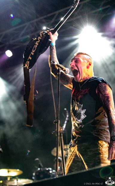 Musician passionately performing on stage, holding a guitar aloft under bright lights.