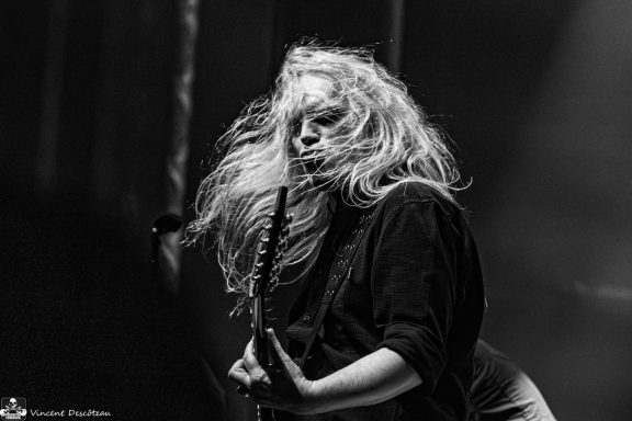 A musician passionately plays guitar with flowing hair in a dramatic black-and-white setting.