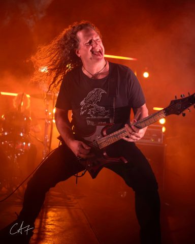 Musician passionately playing electric guitar on stage with dramatic lighting.