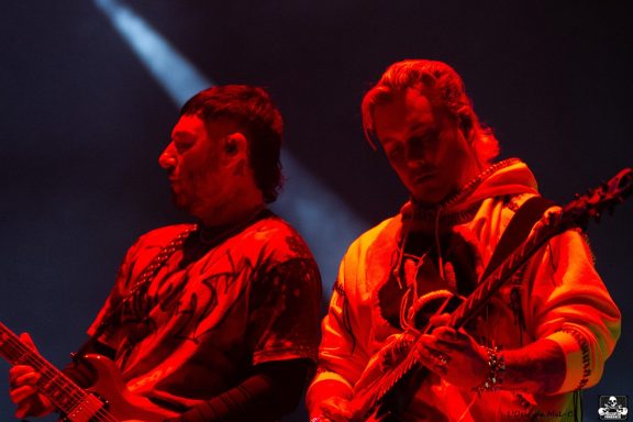 Two musicians performing on stage, illuminated by red and blue lighting.