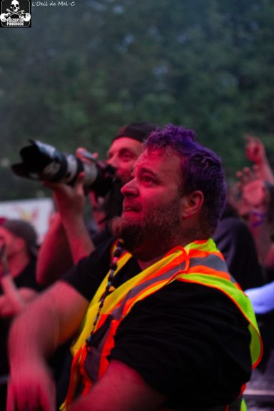 A crowd member with purple hair wearing a safety vest, capturing the event with a camera.