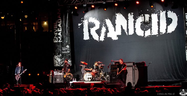 Band Rancid performing on stage with a large backdrop and lights.