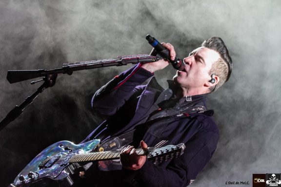 Male vocalist performing onstage with a guitar, shrouded in fog and dramatic lighting.
