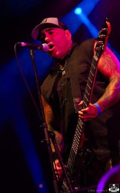 Musician performing live, playing bass guitar under vibrant lighting.