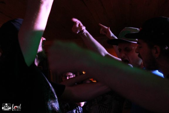 A close-up of people dancing and celebrating with raised arms in a dimly lit venue.