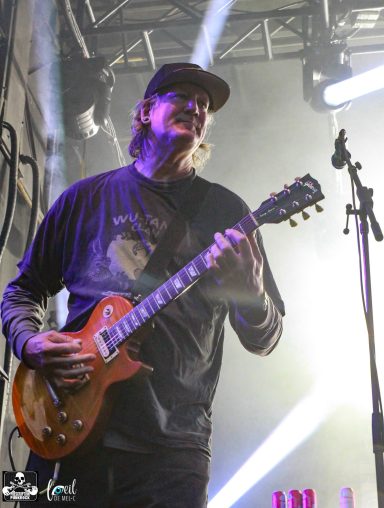 A guitarist in a black shirt playing an electric guitar on stage with lights.