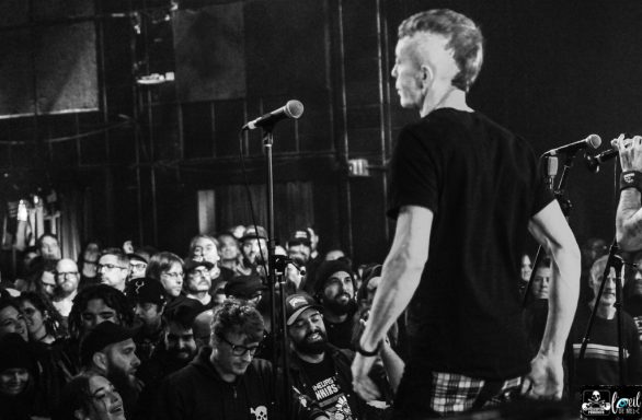 A musician performs on stage, facing a captivated crowd in a dimly lit venue.
