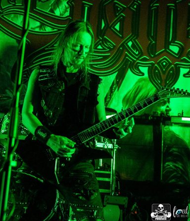 Musician playing electric guitar on stage with green lighting and vibrant background.