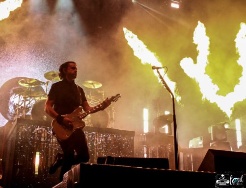 A musician performs on stage with dramatic flames in the background.