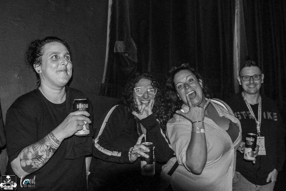 Four people enjoying drinks and smiling, with one playfully covering their face.