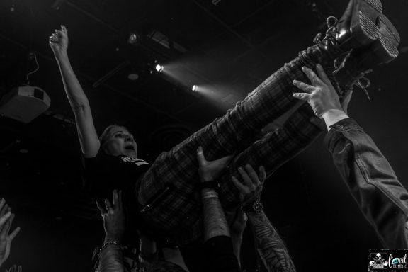 A performer is crowd-surfing, raised by hands in a lively concert setting.