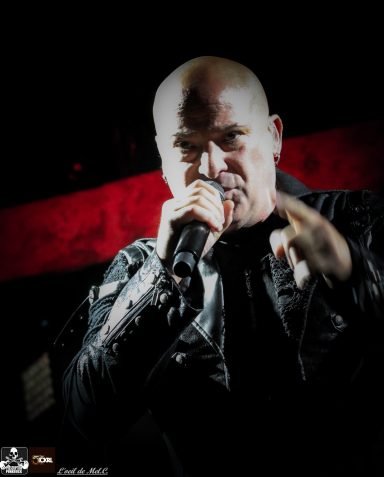 A bald singer in a black jacket passionately performing on stage.